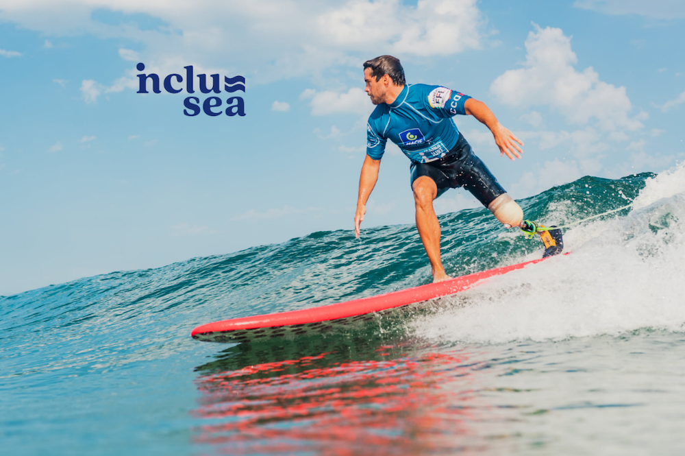 Inclusea adaptive surfing image of a man wearing a shortie wetsuit and blue rash vest with a prosthetic leg surfing an unbroken wave on a red surfboard.